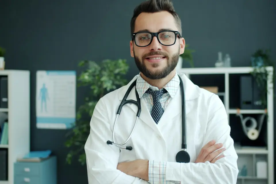 Médico sonriente con bata y estetoscopio en su consulta